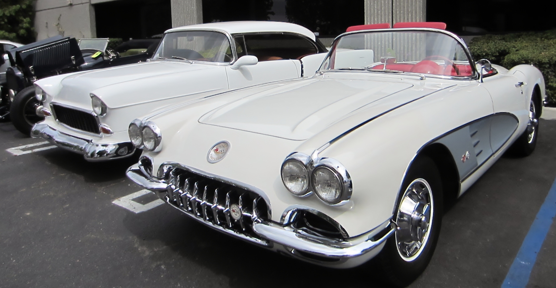 a white early 1960s Corvette parked next to a white 1955 Chevy hot rod