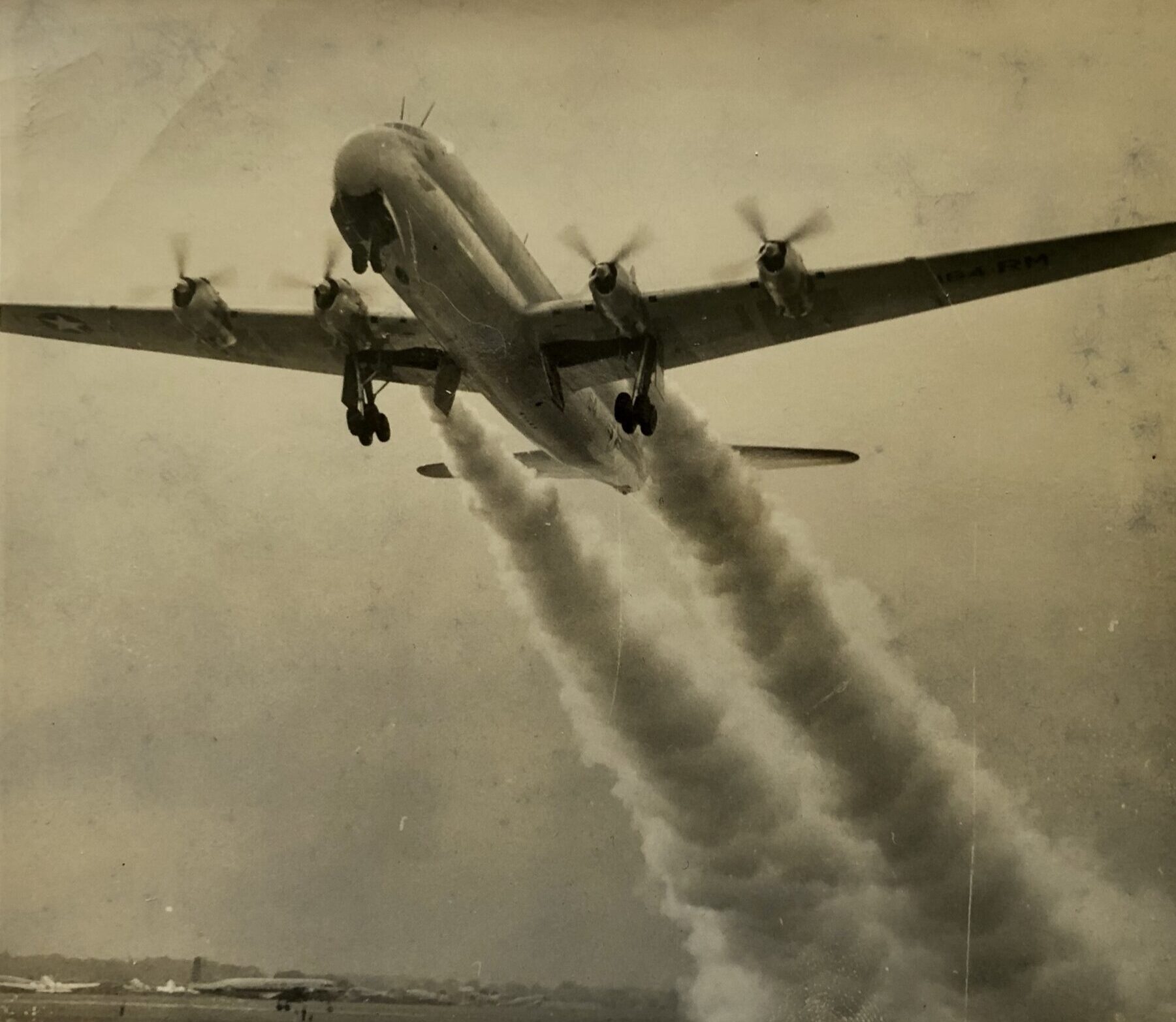 A 1953 black and white image of a Boeing KC 97G Stratofreighter on takeoff, exhaust spewing from its four engines.