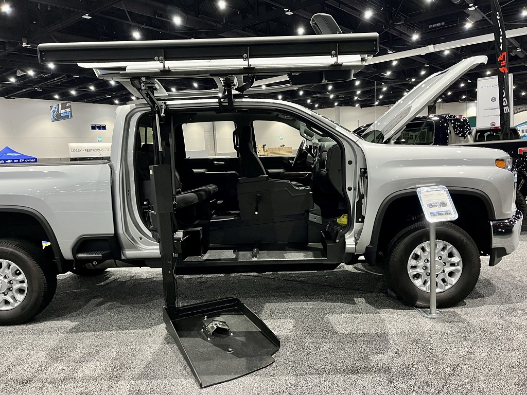 A Golden Boy modified four-door Chevrolet Silverado. Both passenger side doors are open and showing a lift system to the front seats.