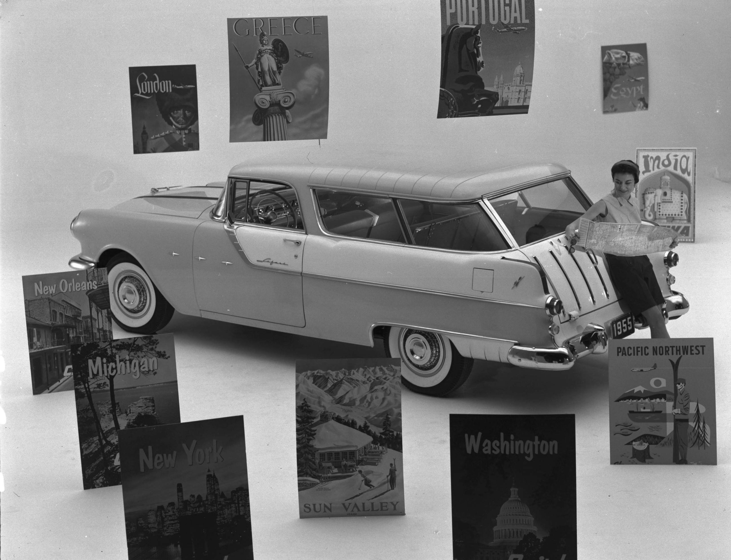 A black and white Safari PR image with large travel posters below and above the car.