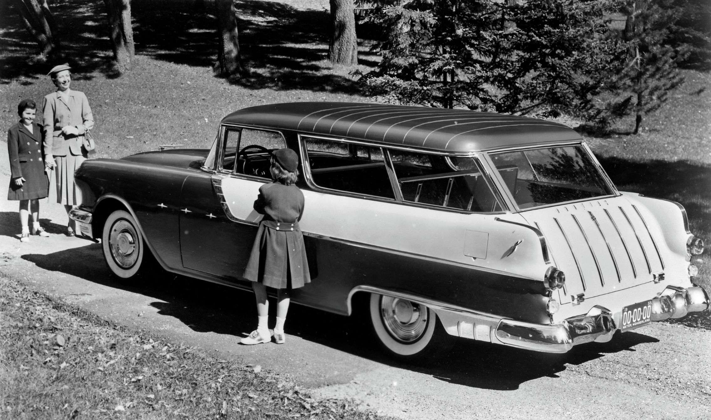 A black and white image of the 1955 Pontiac Safari Chief Custom two door in a home setting with a young girl standing by the driver's closed door