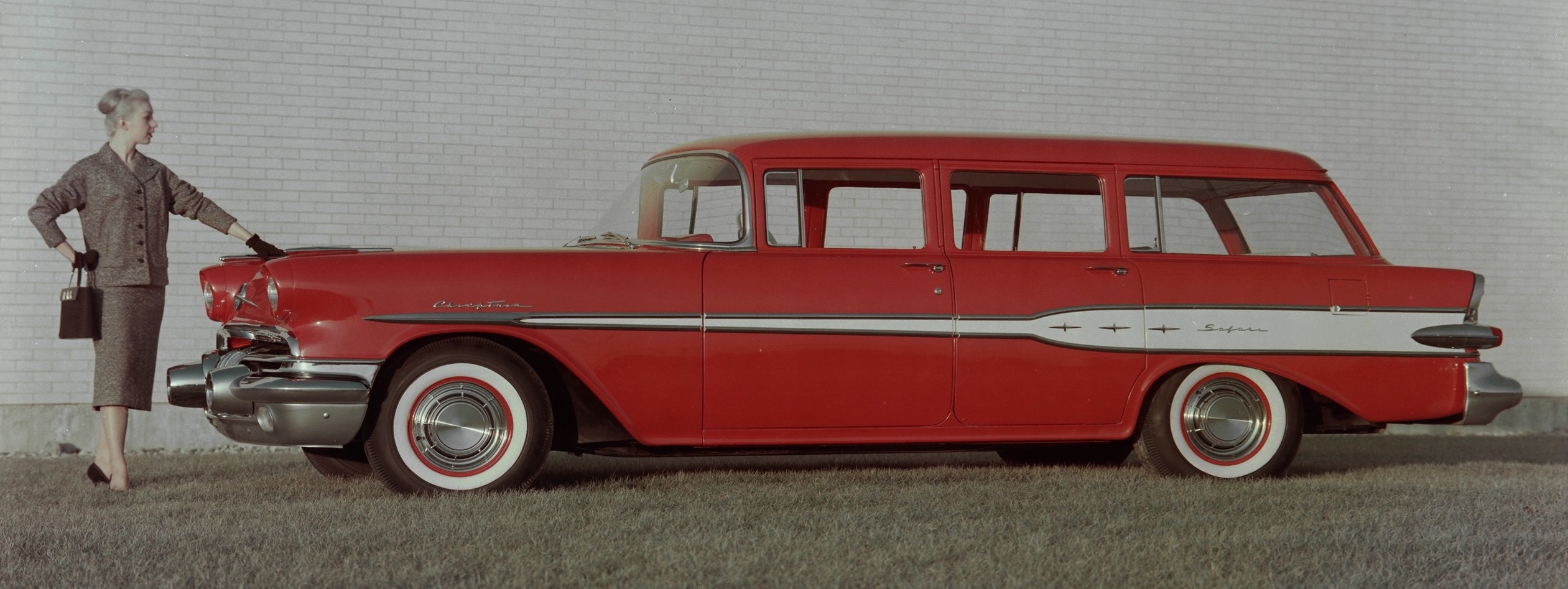 A red 1957 Pontiac Safari four-door wagon with a well dressed woman standing in front